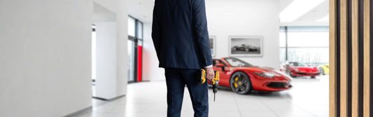 Man in suit standing in a Ferrari dealership with a drill in his hand.