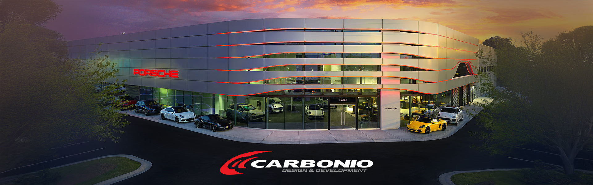 Porsche dealership showroom at sunset with multiple sports cars on display, featuring the Carbonio Design & Development logo in the foreground.